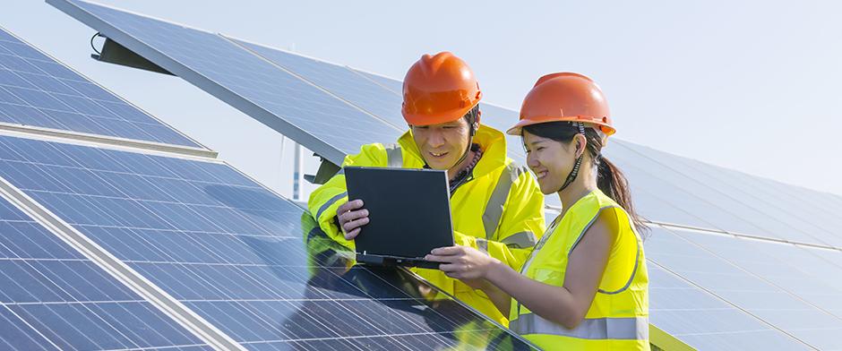 Man and woman reviewing a laptop screen next to a set of industrial-scale solar panels.